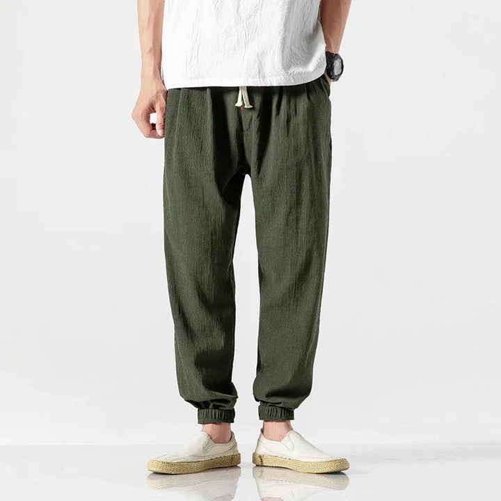 Man wearing casual olive green jogger pants with elastic cuffs and white slip-on shoes