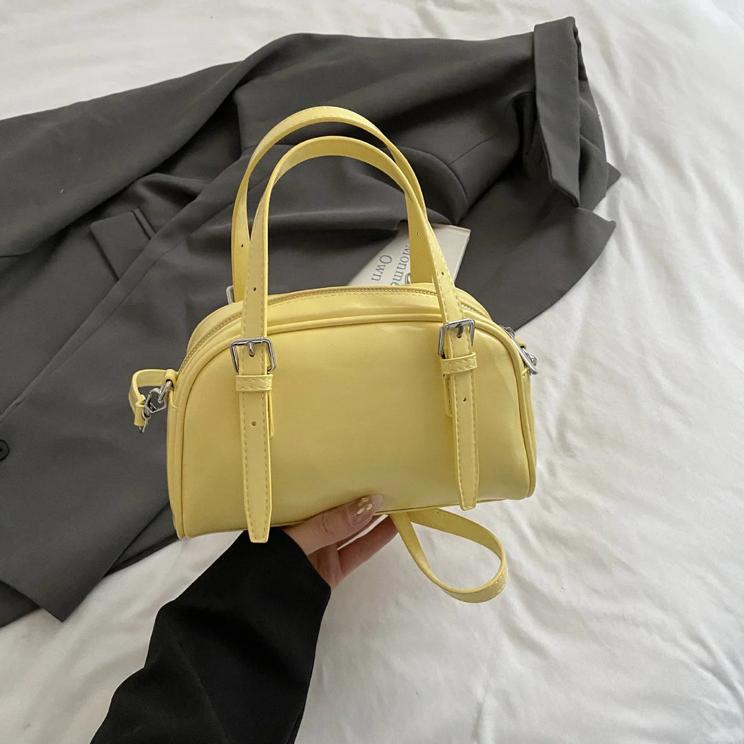 Woman holding small yellow leather handbag over gray blazer on white bed