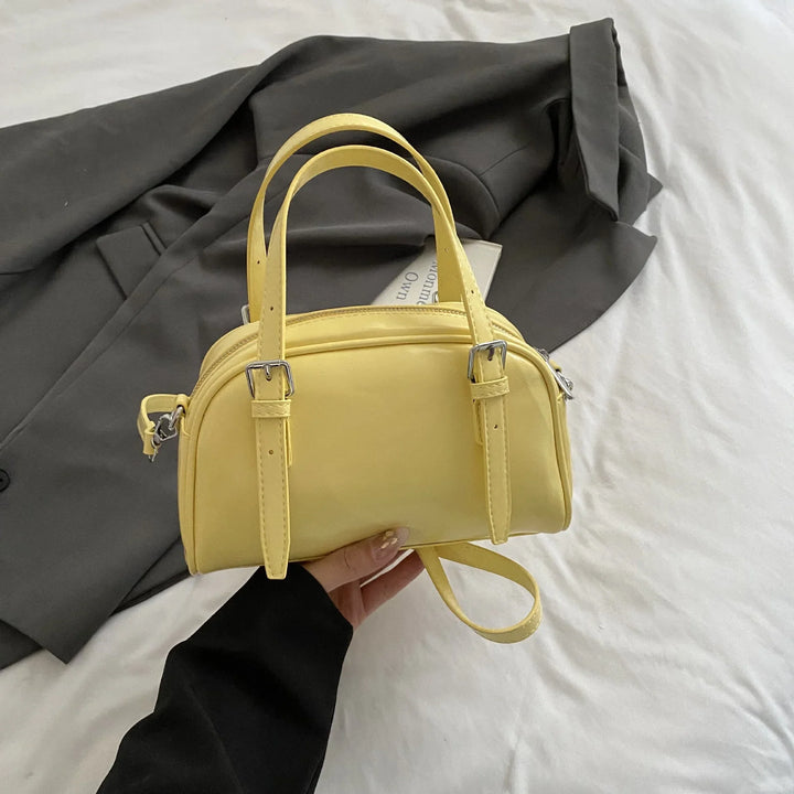 Woman holding small yellow leather handbag over gray blazer on white bed