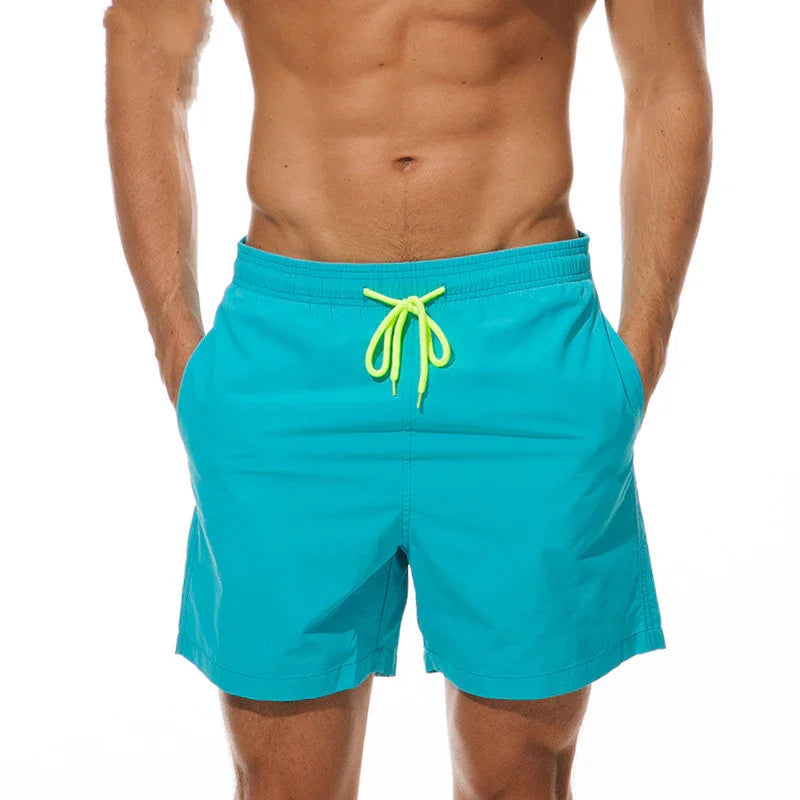 Close-up of man wearing turquoise swim shorts with neon yellow drawstring on white background