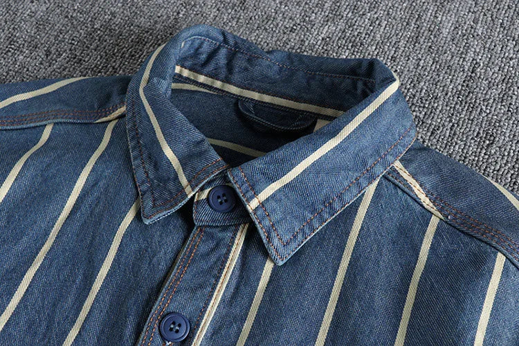 Close-up of a blue denim shirt with white vertical stripes, buttoned collar, and dark blue buttons on a textured gray surface