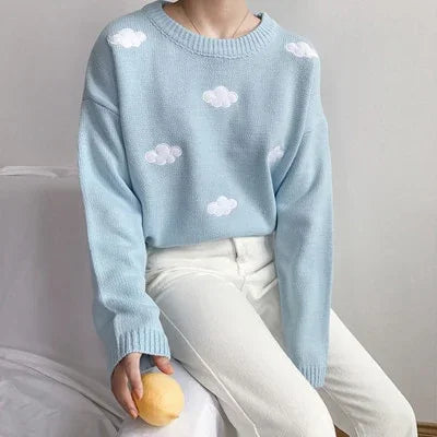 Person wearing light blue sweater with white cloud patterns, paired with white pants, holding a yellow fruit
