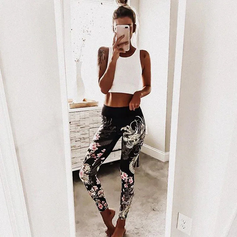 Woman taking mirror selfie wearing white crop top and black leggings with floral and dragon design