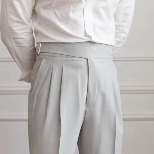 person wearing high-waisted light gray pleated trousers with buckle detail and white shirt