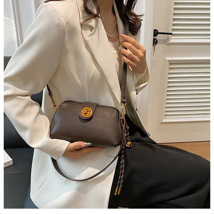 Woman in white blazer holding a dark brown leather crossbody bag with gold clasp and tassel detail