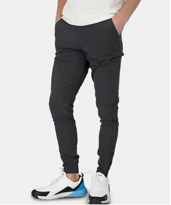 Men's slim fit black joggers paired with white and blue athletic sneakers on plain background
