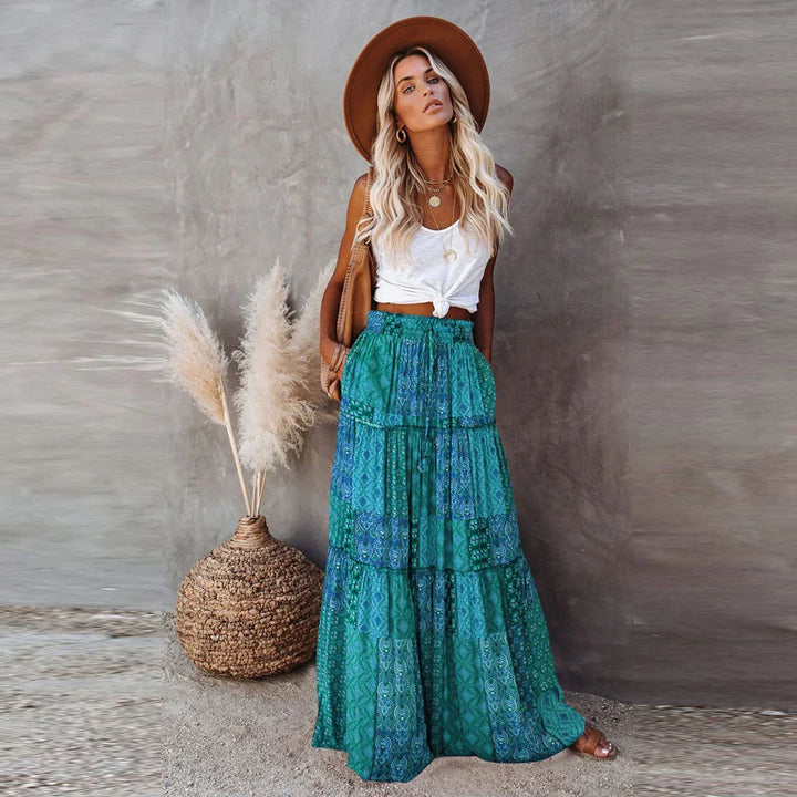 Blonde woman in white knotted tank top and green patterned maxi skirt with brown hat and sandals