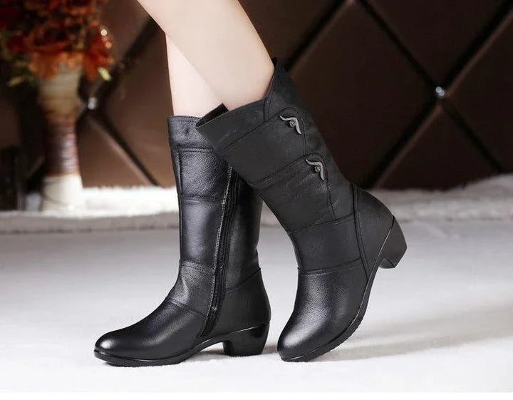 Black mid-calf leather boots with low heels and decorative zippers worn indoors on white floor