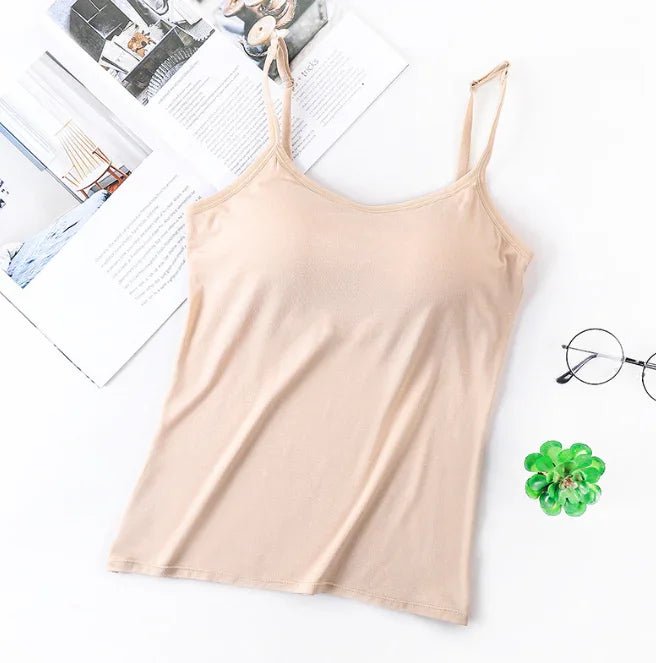 Beige spaghetti strap tank top laid flat on white surface with open book, round glasses, and small green succulent