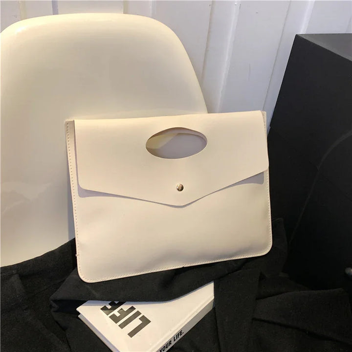 Minimalist cream leather envelope clutch bag on white chair with black fabric and life book
