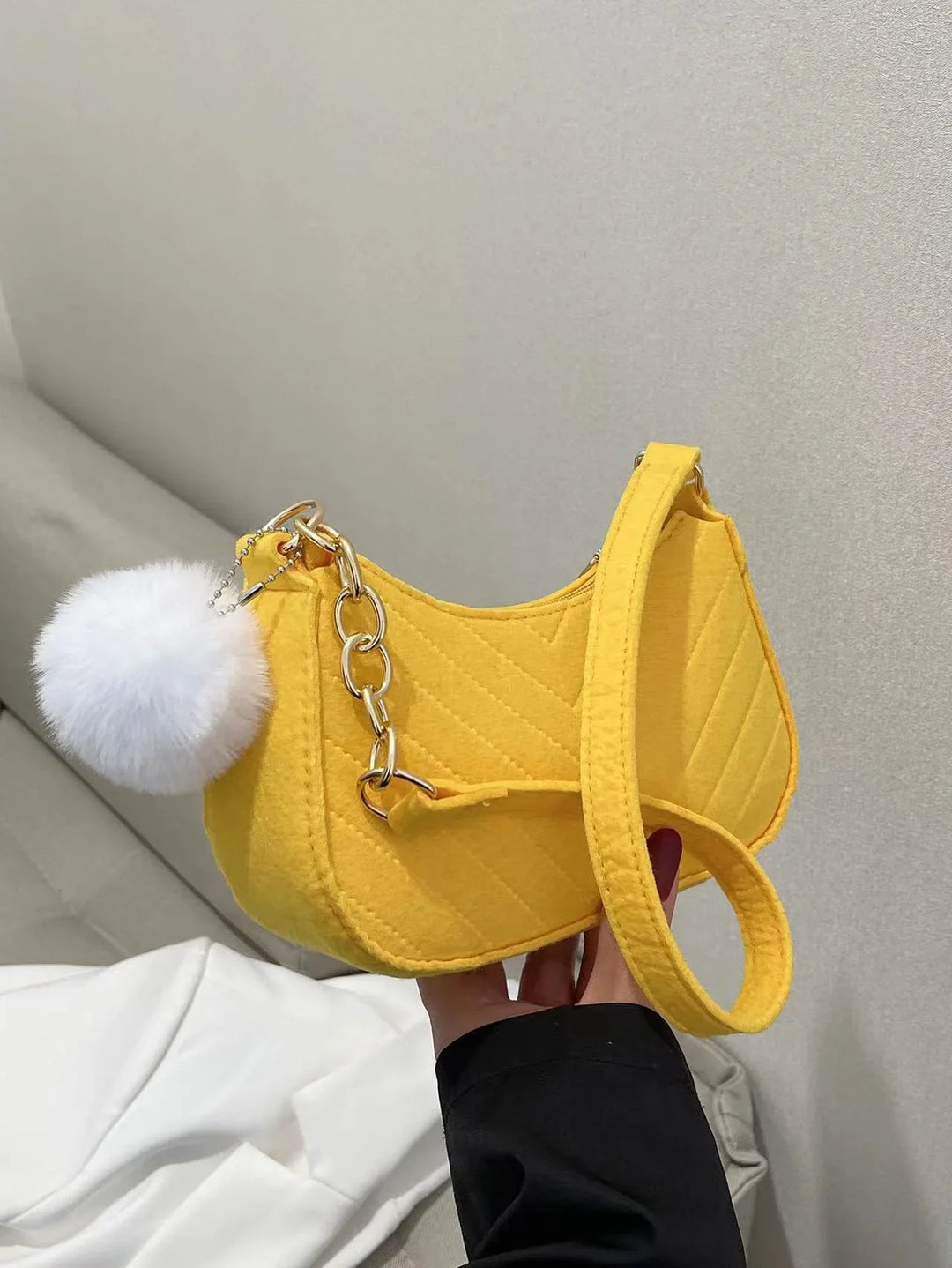 Yellow quilted handbag with gold chain and white fluffy pom-pom charm held indoors
