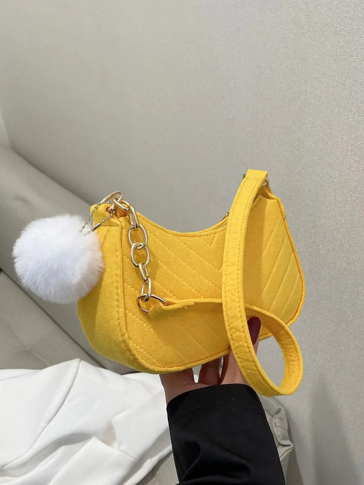 Yellow quilted handbag with gold chain and white fluffy pom-pom charm held indoors
