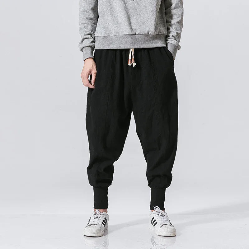 Male model wearing black tapered jogger pants with cuffed ankles and drawstring waist, paired with gray sweatshirt and white sneakers