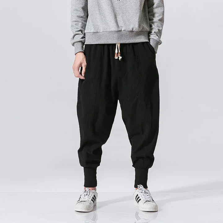 Male model wearing black tapered jogger pants with cuffed ankles and drawstring waist, paired with gray sweatshirt and white sneakers