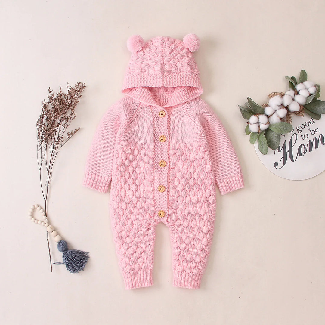 Pink knitted baby onesie with hood and pom-pom ears, wooden buttons, textured pattern