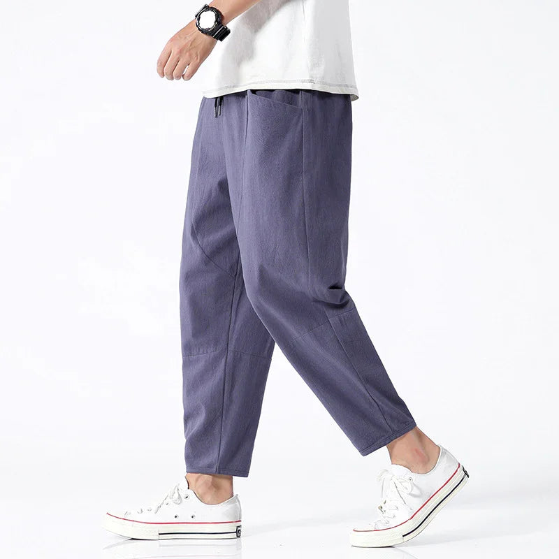 Man wearing casual purple tapered pants with side pockets and white sneakers against white background