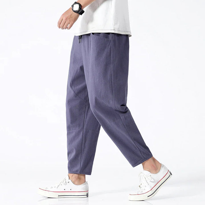 Man wearing casual purple tapered pants with side pockets and white sneakers against white background