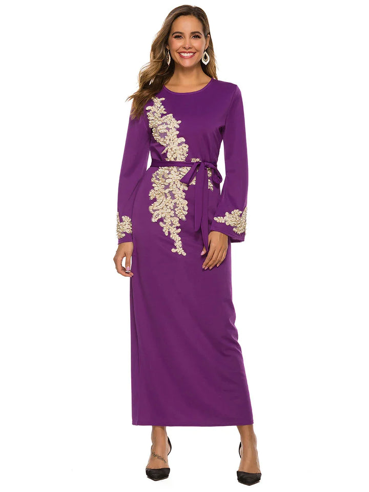 Smiling woman in purple long dress with golden floral embroidery and waist tie, black heels