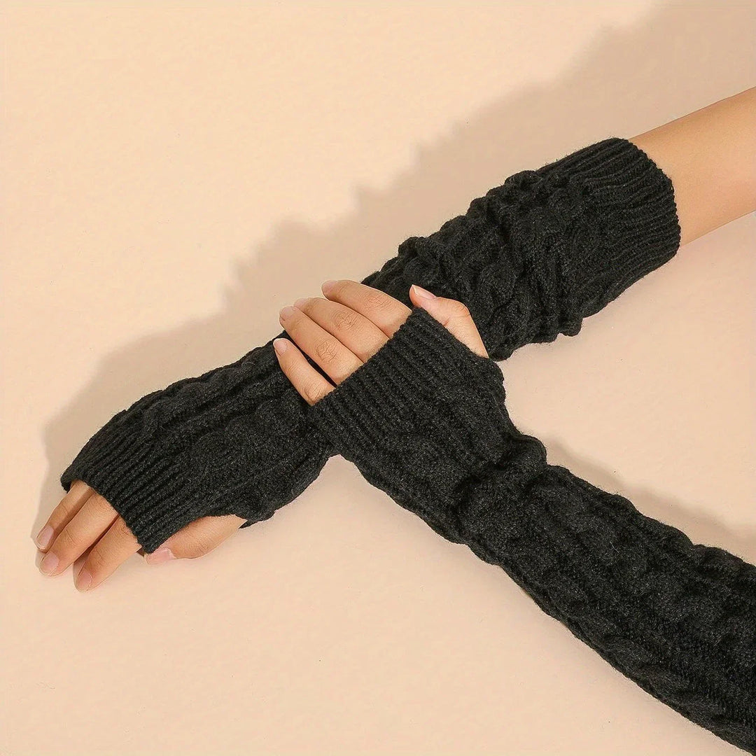Black knitted fingerless arm warmers with cable pattern worn on hands over beige background