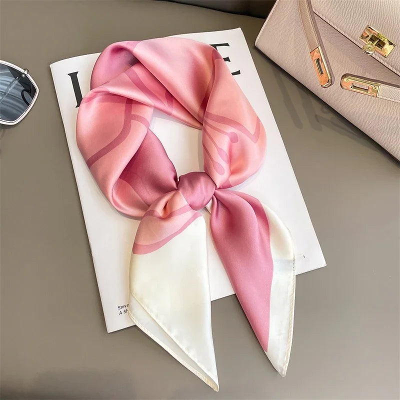 Pink and white silk scarf with abstract design, neatly tied and displayed on magazine with sunglasses and beige handbag nearby