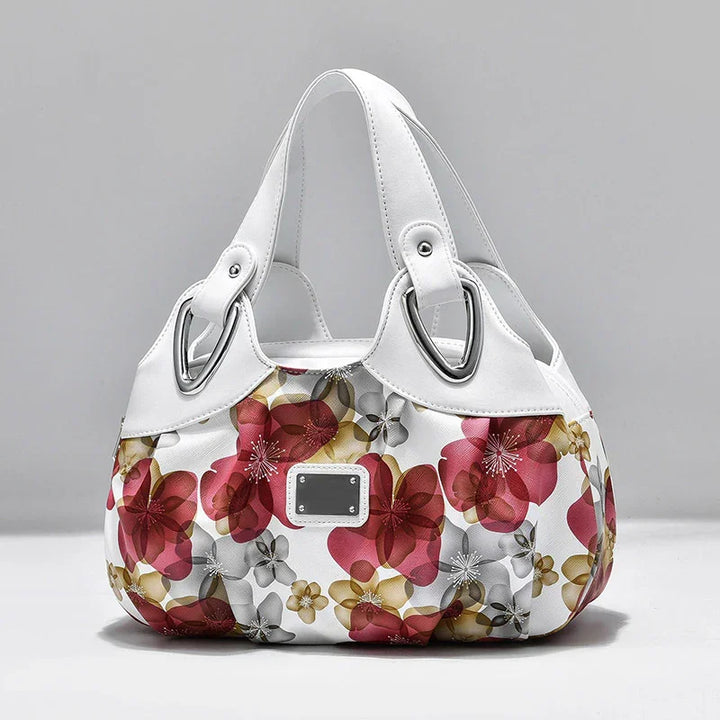 White handbag with large red, gold, and gray floral print and silver hardware details