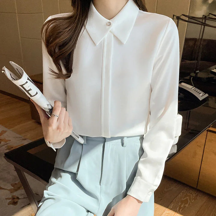 Woman wearing a white long-sleeve blouse with pearl button and light blue high-waisted pants holding rolled magazine