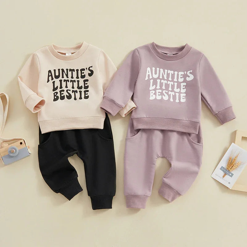 Two toddler outfits with sweatshirts reading 'Auntie's Little Bestie', one beige with black pants, the other mauve with matching pants