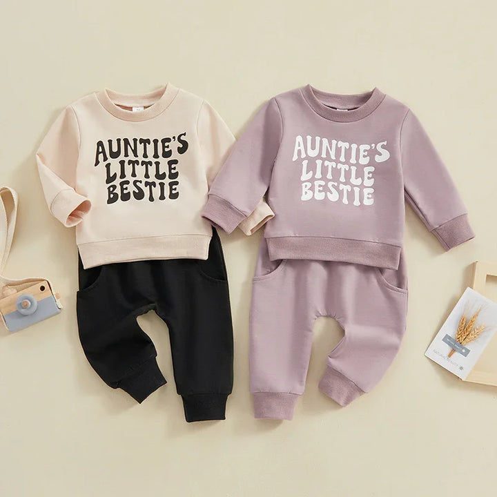 Two toddler outfits with sweatshirts reading 'Auntie's Little Bestie', one beige with black pants, the other mauve with matching pants