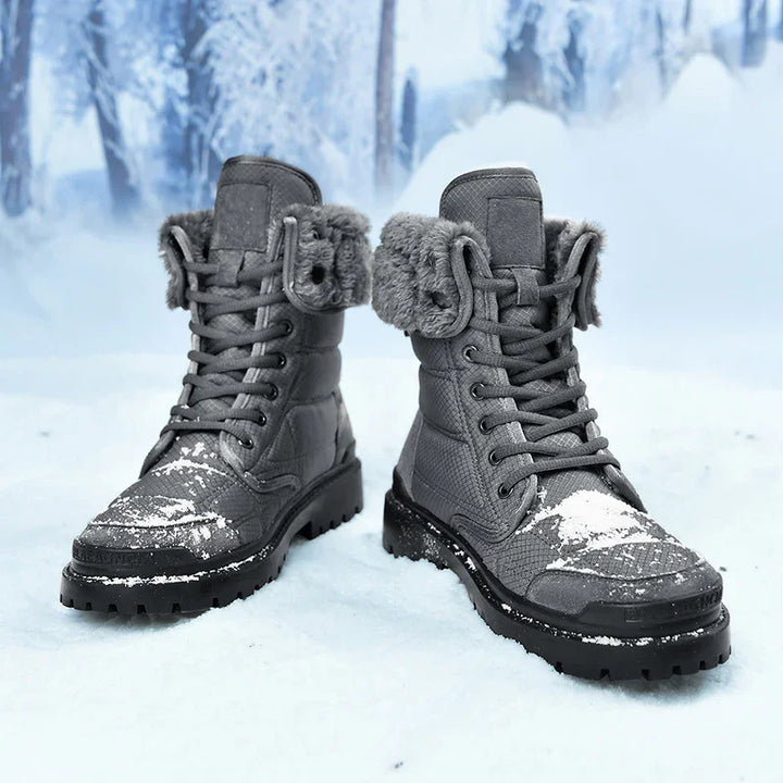 Pair of gray winter boots with fur lining and laces, covered in snow on snowy ground