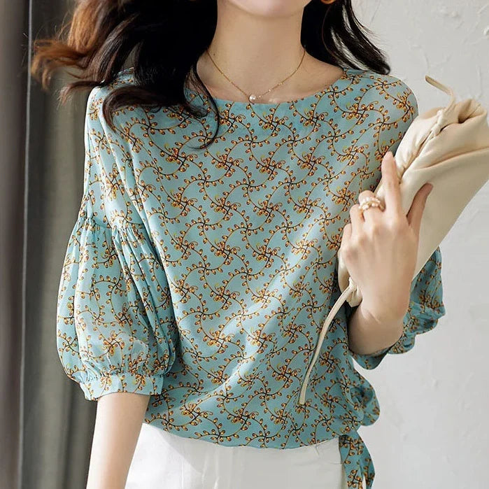 Woman wearing a light blue floral puff sleeve blouse holding a beige clutch bag