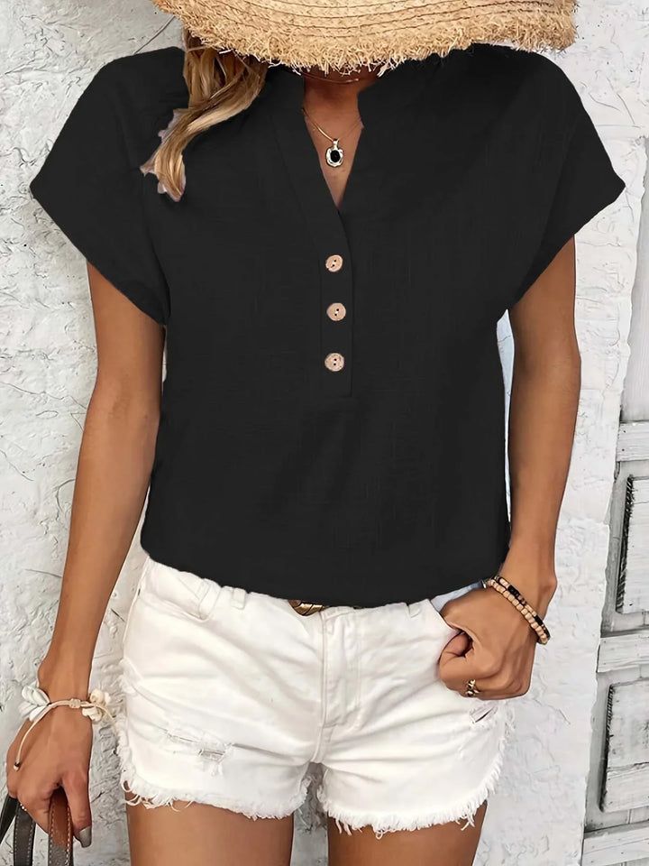 Woman wearing black short sleeve buttoned top and distressed white shorts with straw hat