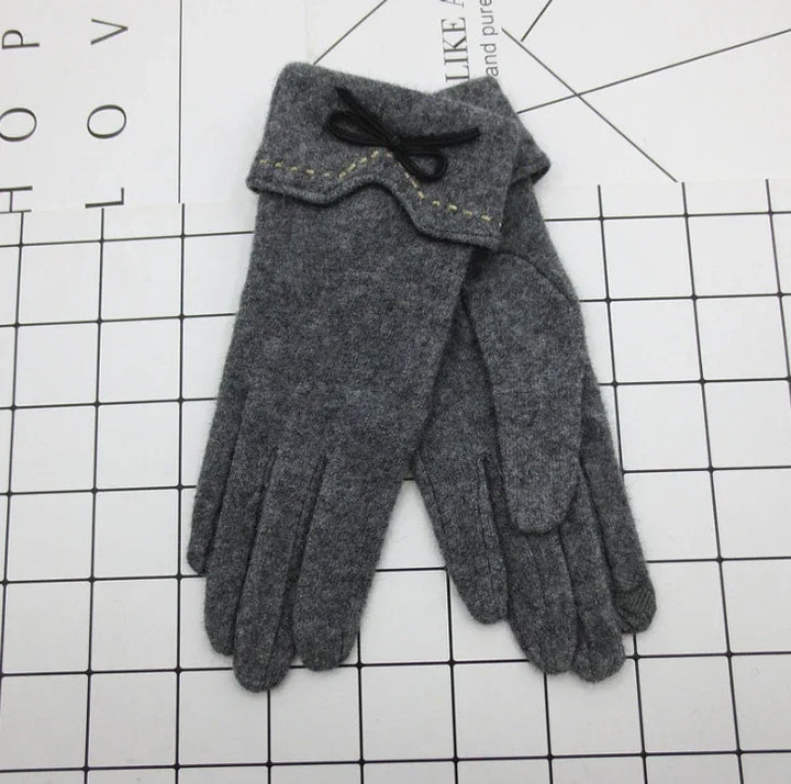 Pair of grey woolen gloves with decorative stitching and black bow detail on cuff