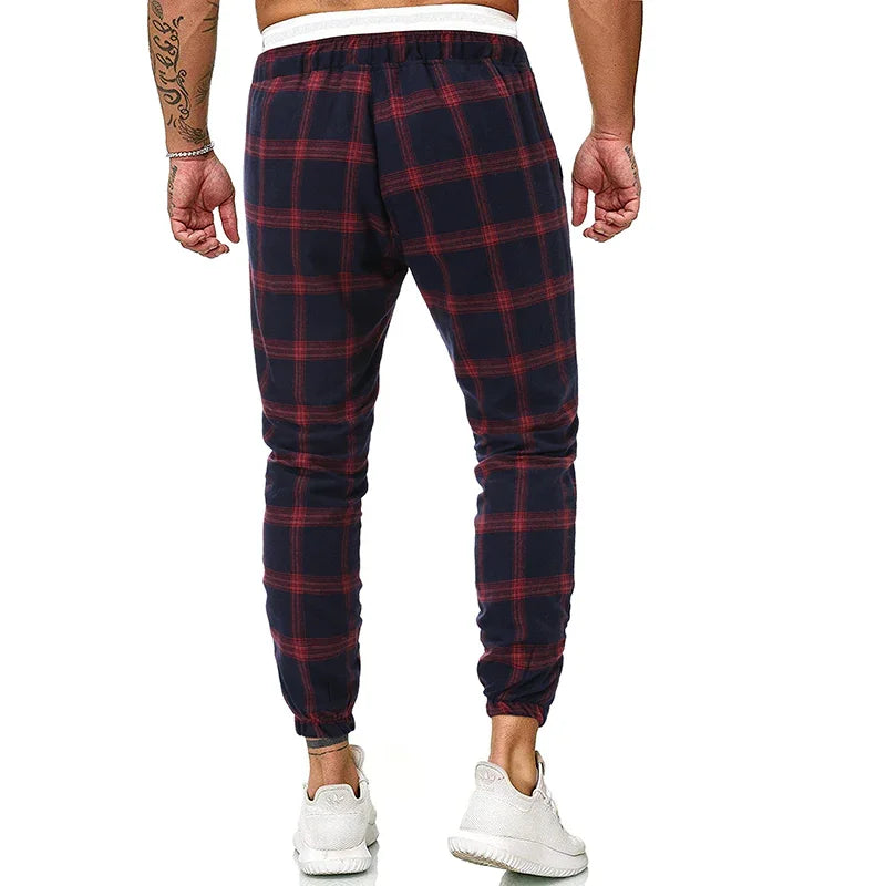 Man wearing navy blue and red plaid jogger pants with white waistband and white sneakers, back view