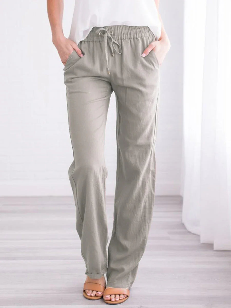 Woman wearing light gray drawstring casual pants with pockets and tan sandals in bright modern room