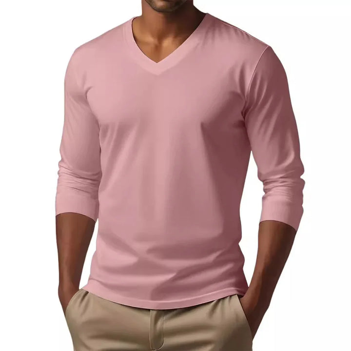 Man wearing a pink V-neck long sleeve shirt with beige pants, hands in pockets