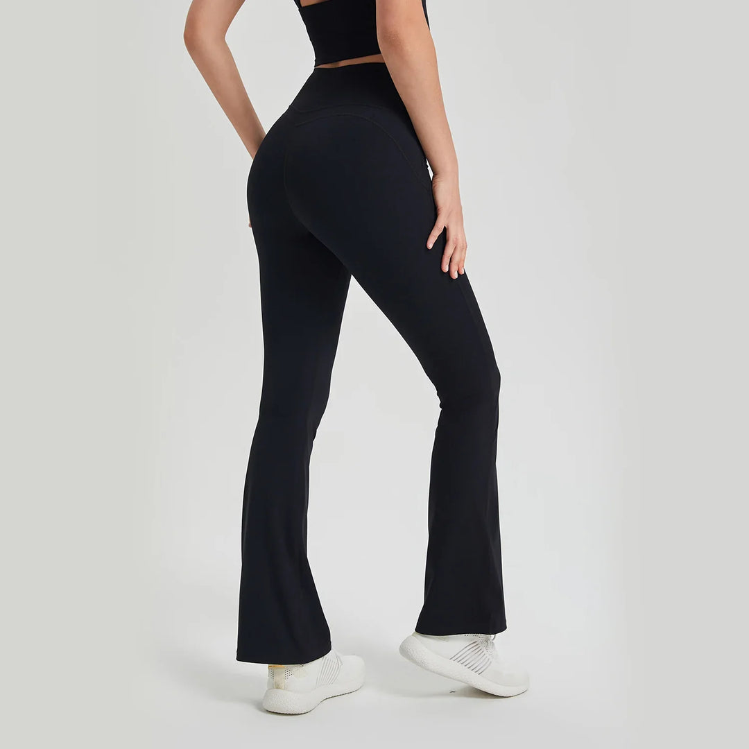 Woman wearing black high-waisted flared yoga pants and white sneakers on neutral background