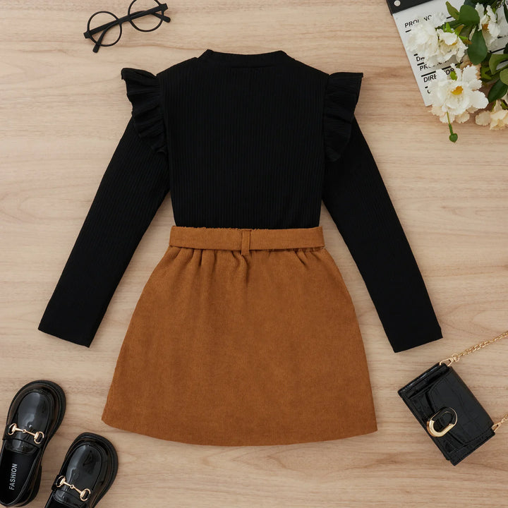 Black long-sleeve top with ruffled shoulders and brown corduroy skirt outfit with black loafers and purse