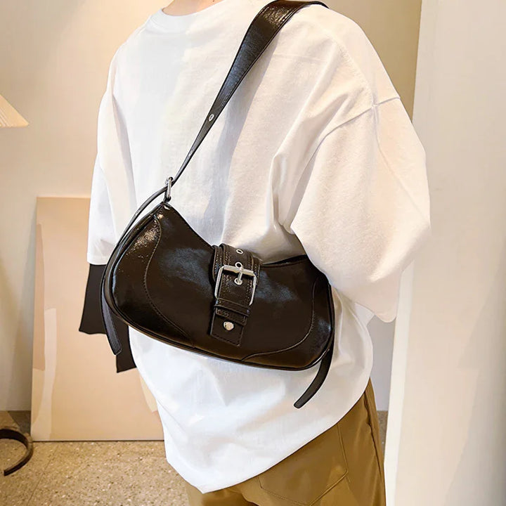 Black leather shoulder bag with silver buckle worn over white t-shirt and brown pants