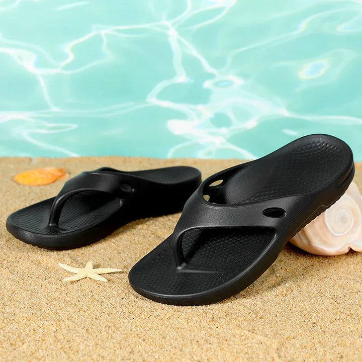 Black flip flop sandals on sandy beach with seashell and starfish near pool water