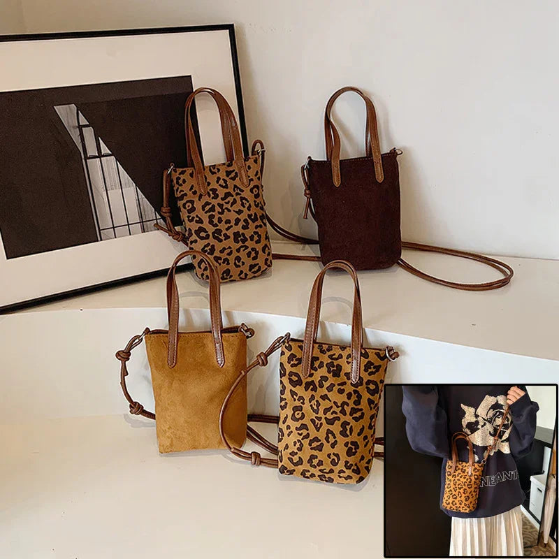 Four small leather crossbody bags in leopard print, brown, and tan on white surface with framed photo
