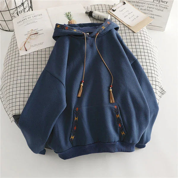 Navy blue hooded sweatshirt with decorative embroidered patterns and tasseled drawstrings on a grid-patterned surface