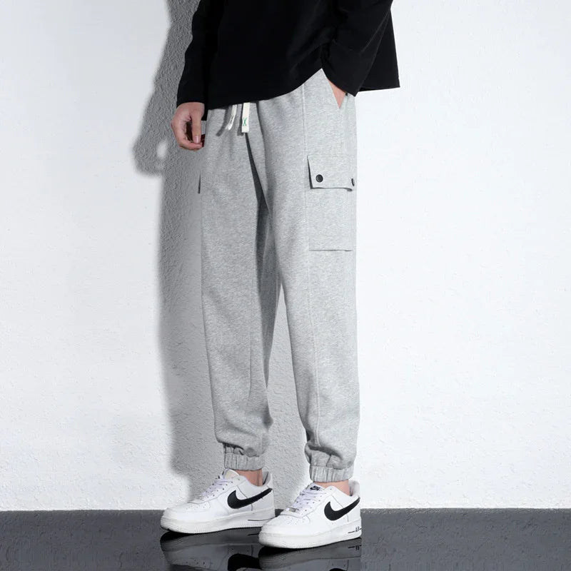 Person wearing light gray cargo jogger pants with elastic cuffs and white Nike sneakers against white wall