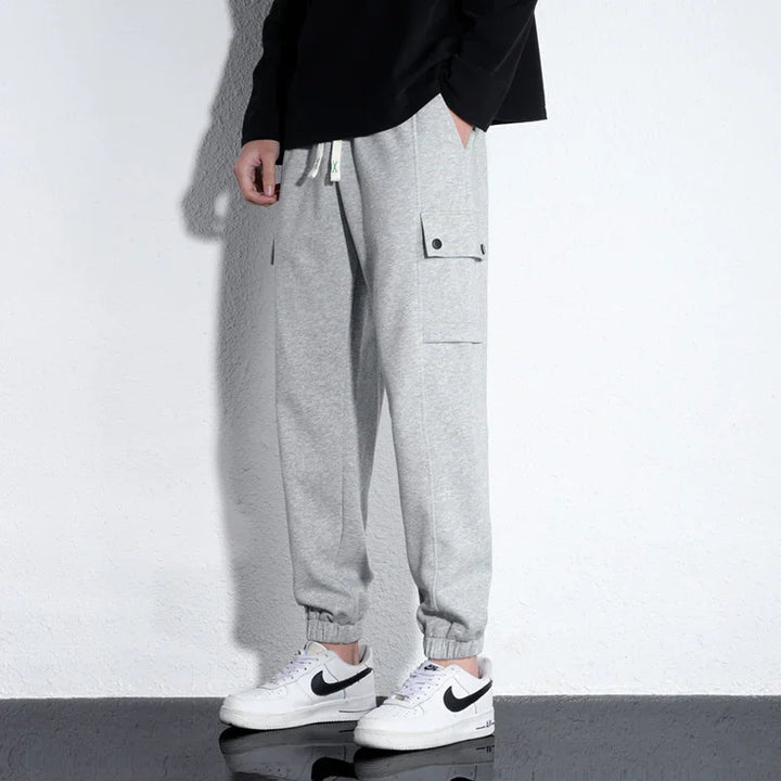Person wearing light gray cargo jogger pants with elastic cuffs and white Nike sneakers against white wall
