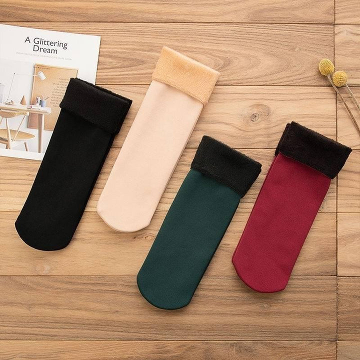 Four folded winter socks in black, beige, green, and red with furry cuffs on wooden surface
