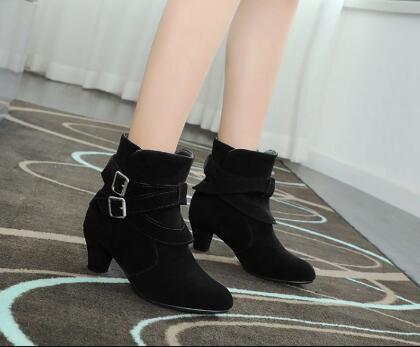 Black suede ankle boots with double buckle straps and block heels worn indoors on patterned carpet