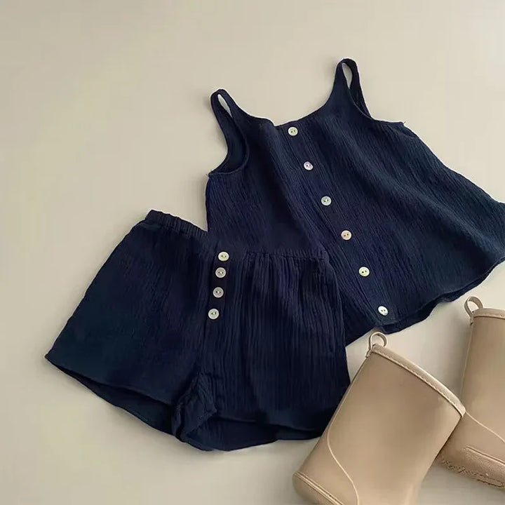 Navy blue sleeveless buttoned top and matching shorts with white buttons, paired with beige boots on beige background