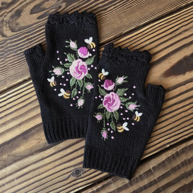 Black knit fingerless gloves with pink rose and bee embroidery on wooden surface