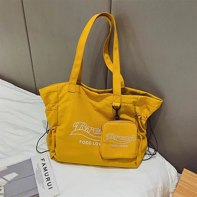 Yellow tote bag with matching small pouch, printed with Bread Food Lover, resting on white bed