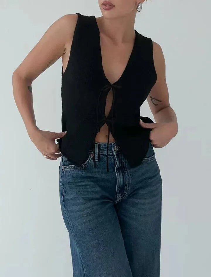 Woman wearing black sleeveless tie-front top and blue high-waisted jeans against plain background
