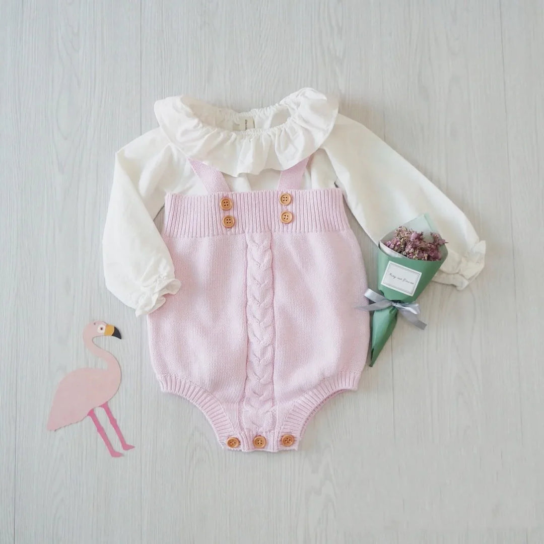 baby outfit with white ruffled collar top and pink knitted romper with wooden buttons on light background